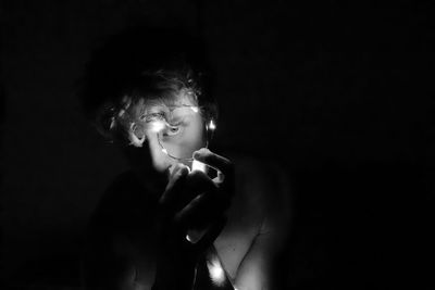 Portrait of man holding illuminated string light in darkroom