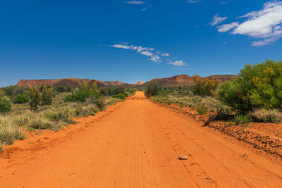 Dirt road along landscape and trees against blue sky