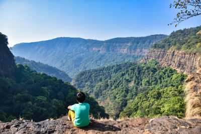 Rear view of boy sitting on mountain against sky