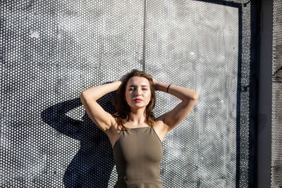 Portrait of beautiful young woman with hand in hair standing against wall