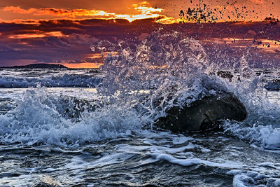 Water splashing in sea against sky during sunset