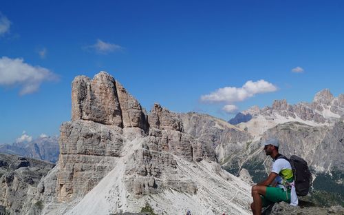 Man sitting on rock by mountain against sky