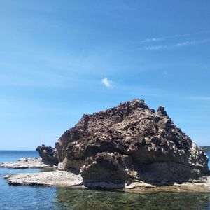 Rock formations by sea against blue sky