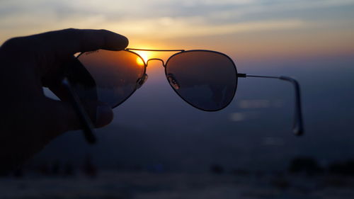 Person holding sunglasses at nandi hills at sunset