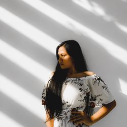 Young woman looking away while standing against wall