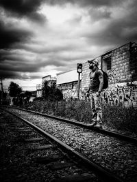 Man standing on railway tracks against cloudy sky