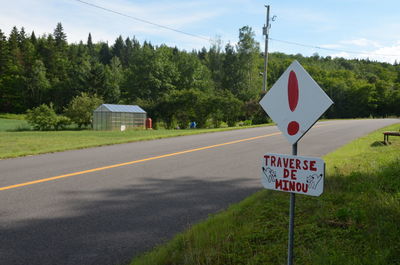 Road sign by trees against sky