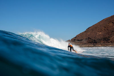 Man surfing in sea against clear blue sky