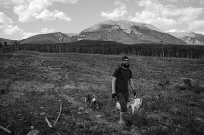 Man walking with dogs on field against mountains