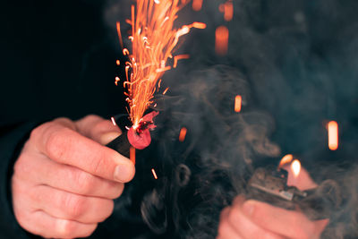Cropped image of hand holding sparkler against fire
