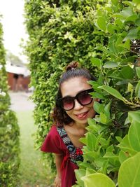 Portrait of smiling woman wearing sunglasses standing amidst plants in park