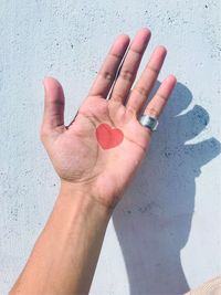 Close-up of hand with heart tattoo on palm against wall