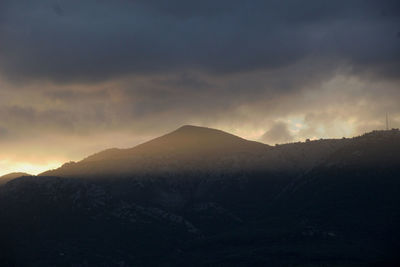 Scenic view of storm clouds over mountain during sunset