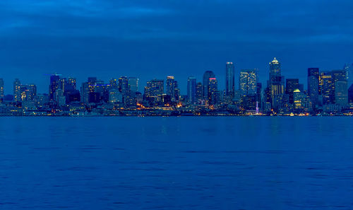 Illuminated buildings by sea against blue sky