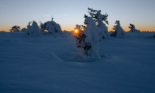 Snow covered land against sky during sunset