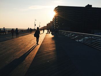 Silhouette people walking on bridge in city during sunset
