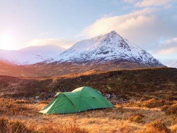 Green touristic tent on meadow at river below snowy cone of stob dearg 1021 metres high. hikers tent