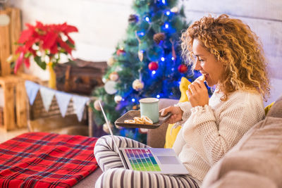 Woman eating food while using laptop during christmas at home