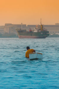 Rear view of man in sea against sky during sunset