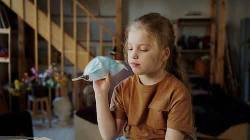 Cute girl holding mask while sitting at home