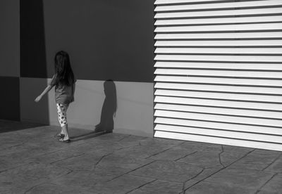 Rear view of girl walking on sidewalk by wall