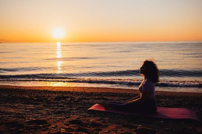 Silhouette woman standing at beach against sky during sunset