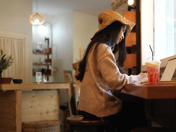 Young woman working on laptop by milkshake at cafe