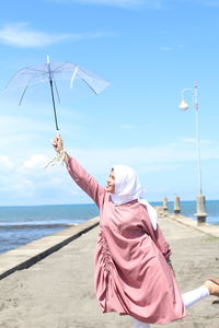 Woman holding umbrella by sea on walkway