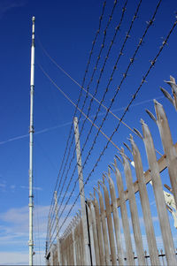 Low angle view of communications tower and security fence against blue sky