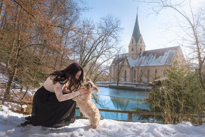 Woman with dog on snow covered field by lake
