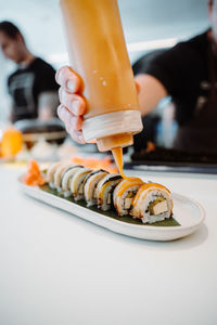 Vertical view of the hands of unknown chief decorating tasty rolls with japanese mayonnaise sauce