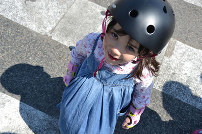 High angle portrait of cute smiling girl wearing sports helmet standing at playground during sunny day