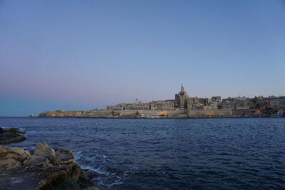 View of sea and buildings against clear blue sky
