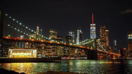 Illuminated brooklyn bridge over river in city at night