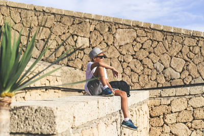 Full length of boy sitting by stone wall