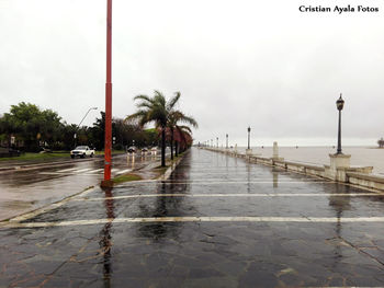 Wet sidewalk by sea against sky