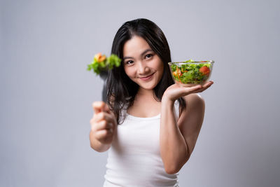 Portrait of smiling young woman holding ice cream against gray background