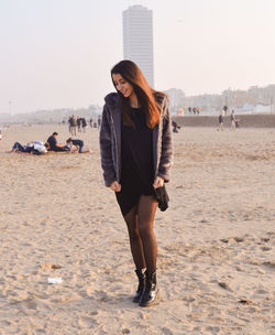 Full length of young woman wearing jacket while standing at sandy beach
