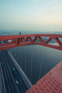 Man standing on railing over river against sky