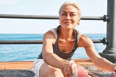 Fit woman relaxes on seaside promenade after running and training on a road by the sea. 