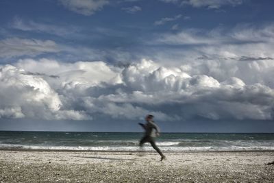 Blurred motion of man running at beach against sky