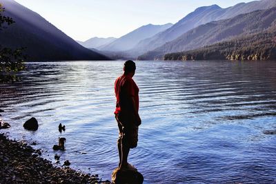 Side view of man standing on rock by lake against mountains