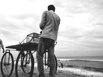 Rear view of man standing on beach against sky