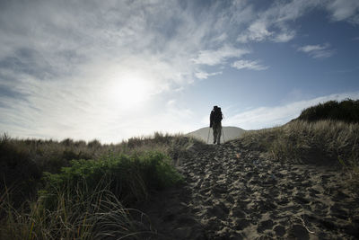 Rear view of man walking on field against sky