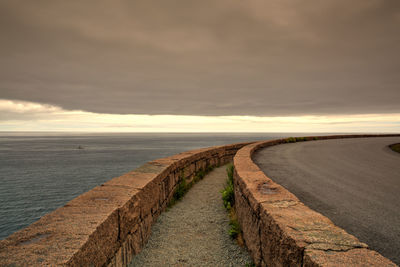 Empty road by sea against sky during sunset