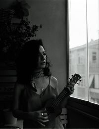 Young woman playing guitar at window