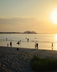 Silhouette people on beach against sky during sunset