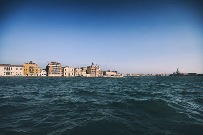 View of buildings by sea against clear blue sky