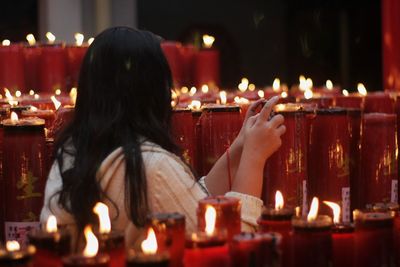 Rear view of woman against illuminated candles in temple