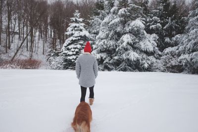 Rear view of man with dog walking on snow